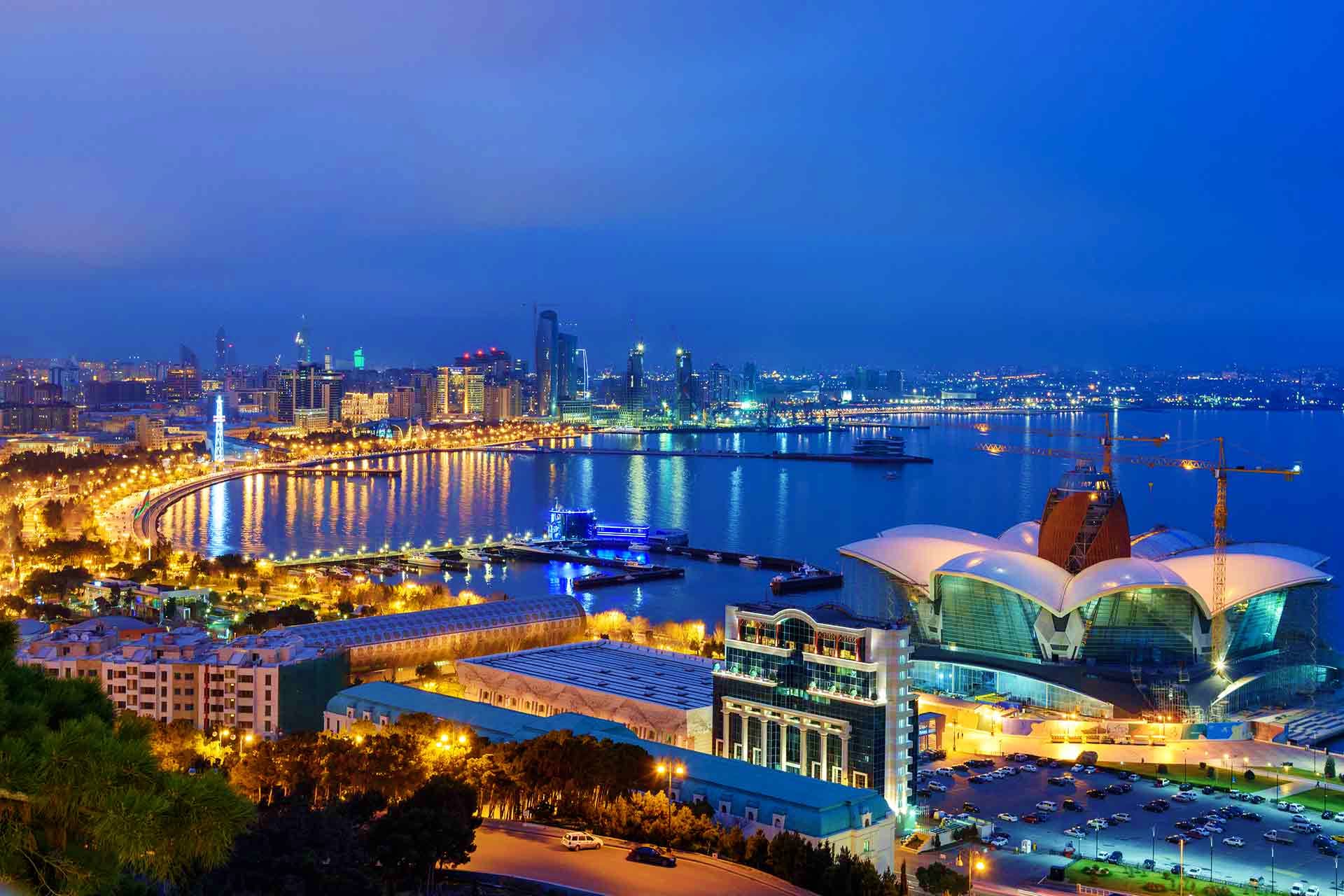 Baku cityscape at dusk with illuminated waterfront, modern buildings, and Heydar Aliyev Center's distinctive white architectu